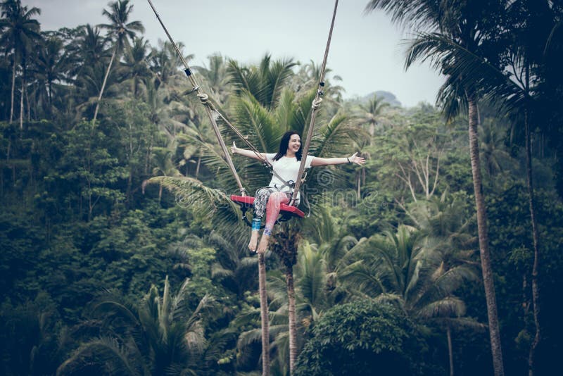 BALI, INDONESIA - 26 DICEMBRE 2017: Donna divertendosi un'oscillazione nella giungla Donna che oscilla nella foresta pluviale di immagine stock BALI, INDONESIA - 26 DICEMBRE 2017: Donna divertendosi un'oscillazione nella giungla Donna che oscilla nella foresta pluviale di immagine stock