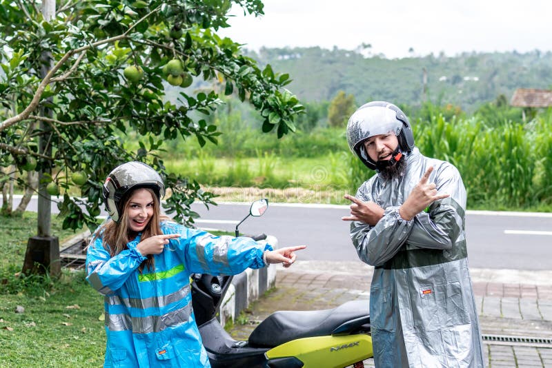 BALI, INDONESIA - JANUARY 3, 2019: Young couple in raincoats with scooter on a nature background having fun.