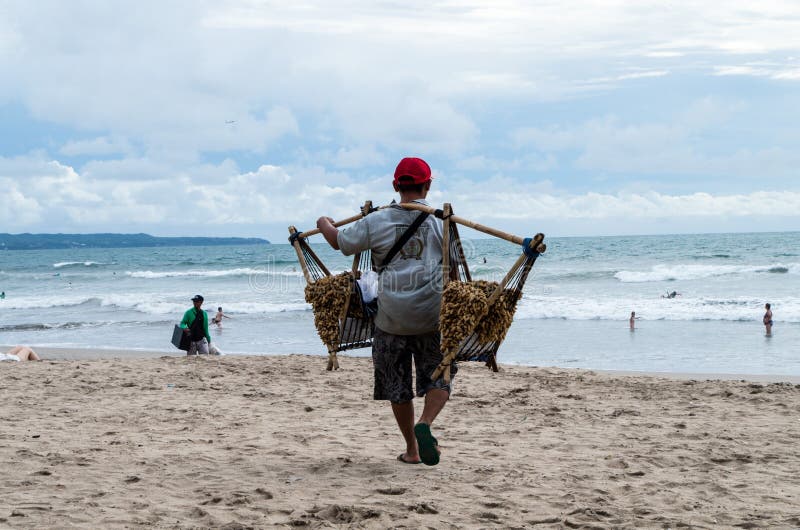 BALI, INDONESIË JANUARI 2017: De pindaverkoper loopt langs Kuta-strand en probeert om lokale pinda's aan toeristen te verkopen stock afbeeldingen BALI, INDONESIË JANUARI 2017: De pindaverkoper loopt langs Kuta-strand en probeert om lokale pinda's aan toeristen te verkopen stock afbeeldingen