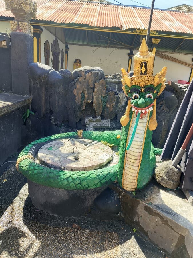 A Balinese serpent statue wraps around a traditional well in a temple courtyard. stock photos