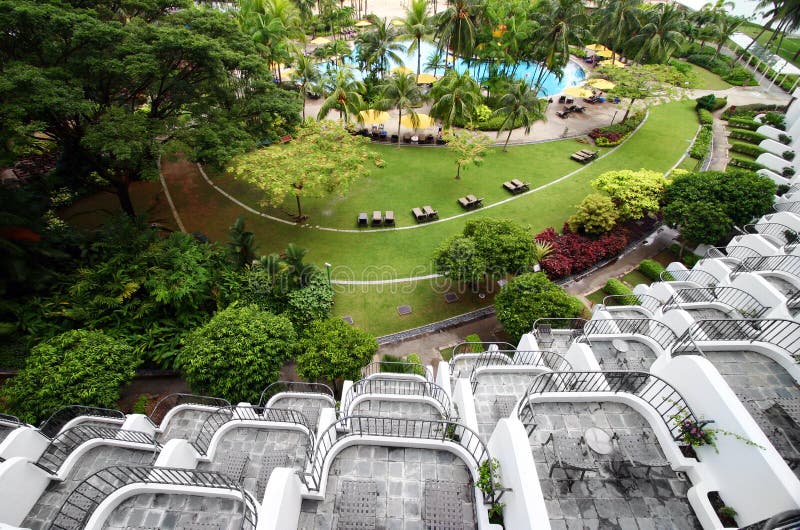 An image showing the many storeys of curved balconies of a resort building. Balcony overlook landscaped garden with swimming pool and lush tropical plants. Deck chairs can be seen in gardens and along swimming poolside. Outdoors furniture on balconies. Interesting architectural feature. Horizontal color format, nobody in picture. An image showing the many storeys of curved balconies of a resort building. Balcony overlook landscaped garden with swimming pool and lush tropical plants. Deck chairs can be seen in gardens and along swimming poolside. Outdoors furniture on balconies. Interesting architectural feature. Horizontal color format, nobody in picture.