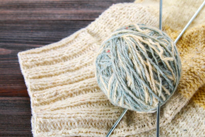 A ball of wool with knitting needles and knitted socks on a wooden table. Needlework.