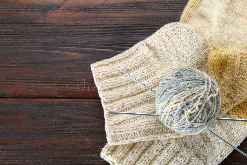 A ball of wool with knitting needles and knitted socks on a wooden table. Needlework.