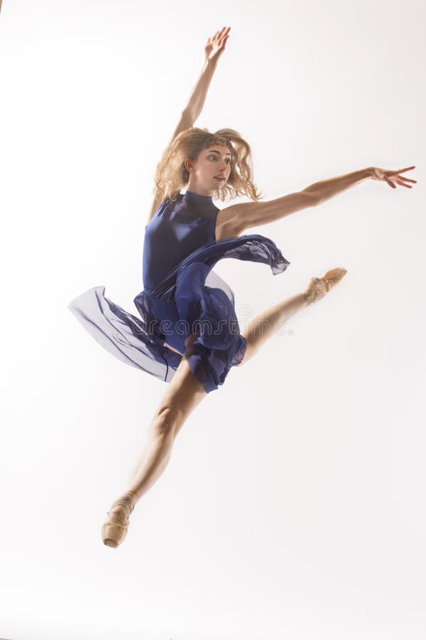 Young woman ballet dancer in pointe shoes,blue leotard and skirt, leaping in the studio against a white background. Young woman ballet dancer in pointe shoes,blue leotard and skirt, leaping in the studio against a white background