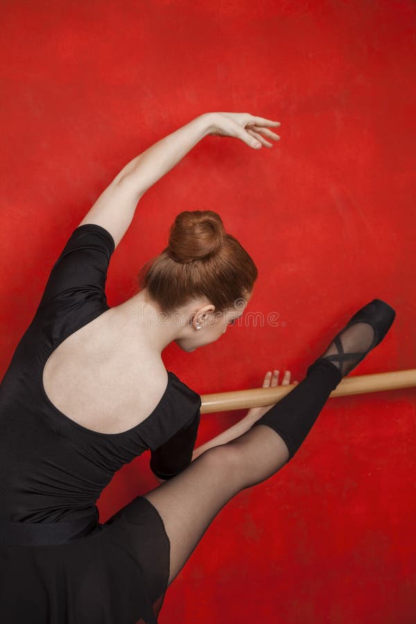 Ballerina che allunga a Barre Against Red Wall fotografia stock Ballerina che allunga a Barre Against Red Wall fotografia stock