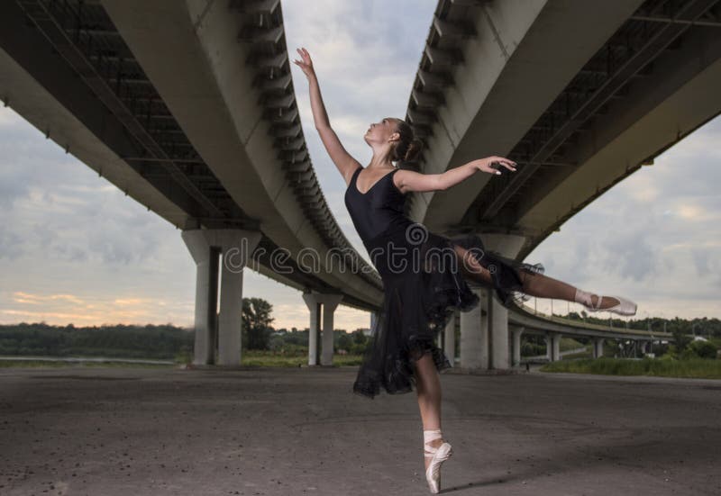 Ballerina i den svarta dräkten som poserar på tår, brobakgrund royaltyfria foton Ballerina i den svarta dräkten som poserar på tår, brobakgrund royaltyfria foton