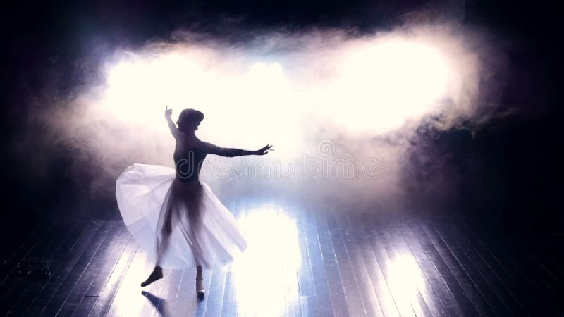 A ballerina jumps through a dark wooden stage.