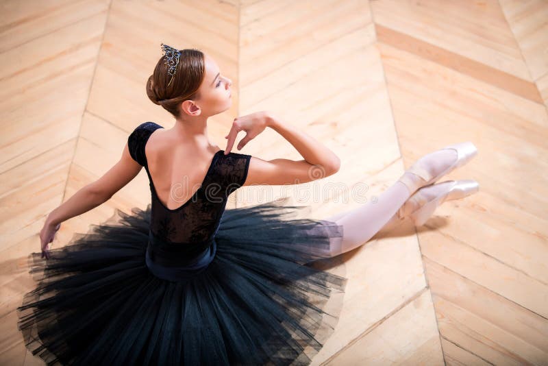 Ballerina in un tutu nero seduto sul pavimento con la schiena rivolta alla telecamera