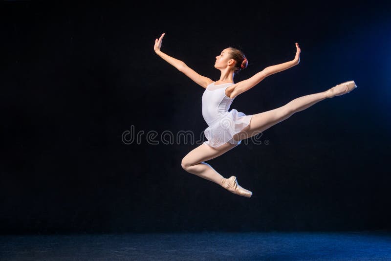 Ballerina in un volo bianco del vestito in un salto su fondo nero