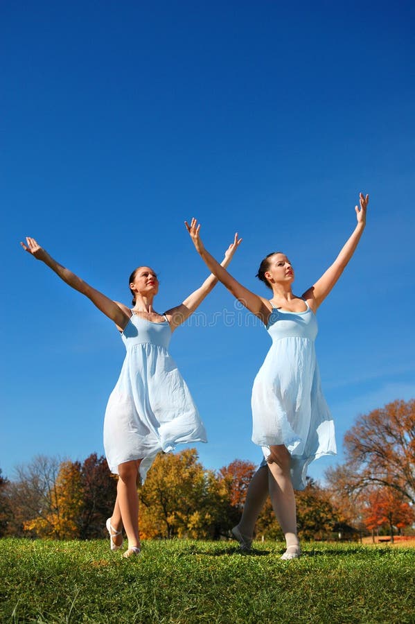 Ballerinas dancing outdoors with arms raised over a colorful background.