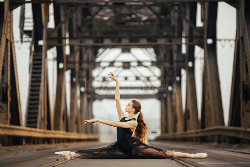 Ballerine s'asseyant dans la pose de ficelle sur la route et les rails à côté des appuis en métal image libre de droits Ballerine s'asseyant dans la pose de ficelle sur la route et les rails à côté des appuis en métal image libre de droits