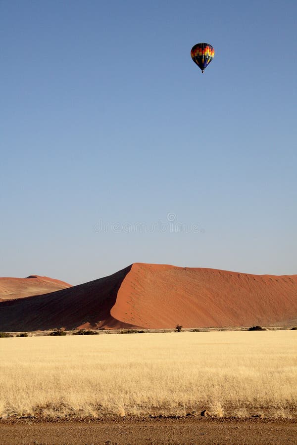 An Air balloon flies over a red dune in the Namib Desert - Namibia. The picture is taken in the early morning and the whole image shows a golden meadow. An Air balloon flies over a red dune in the Namib Desert - Namibia. The picture is taken in the early morning and the whole image shows a golden meadow.