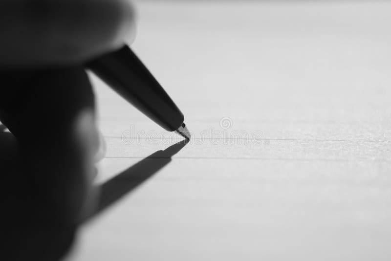 Ballpoint pen in fingers on notebook paper in line. Macro photo, side view. Black and white photo.