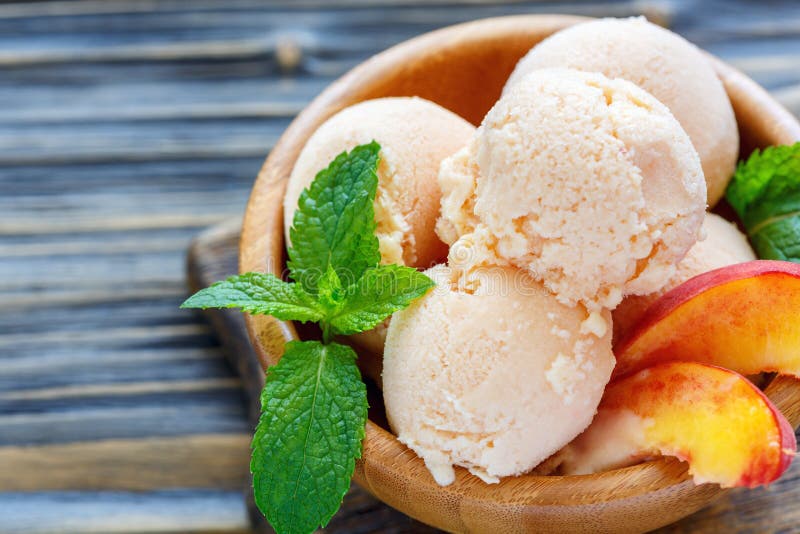 Peach ice cream, mint leaves and slices of fresh peaches in a wooden bowl, selective focus. Peach ice cream, mint leaves and slices of fresh peaches in a wooden bowl, selective focus.