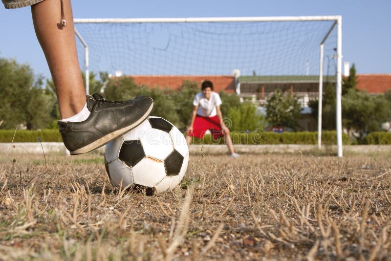 An amateur player is going to shoot a penalty to the goal on a poor soccer pitch. An amateur player is going to shoot a penalty to the goal on a poor soccer pitch