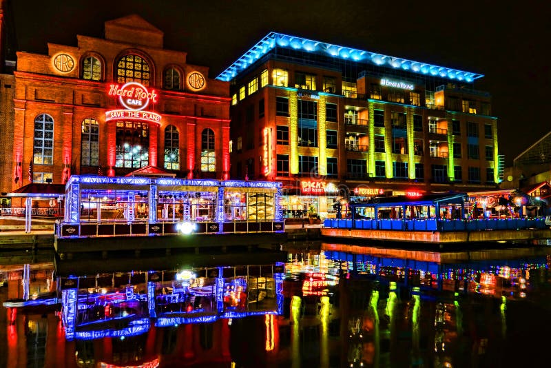 Hard Rock Cafe restaurant and music theme entertainment bar with commercial waterfront building and stores lit by bright colored lights and colorful neon signs reflections in the water on Baltimore Pier 4 Harbor Bridge Walk at night. Hard Rock Cafe restaurant and music theme entertainment bar with commercial waterfront building and stores lit by bright colored lights and colorful neon signs reflections in the water on Baltimore Pier 4 Harbor Bridge Walk at night