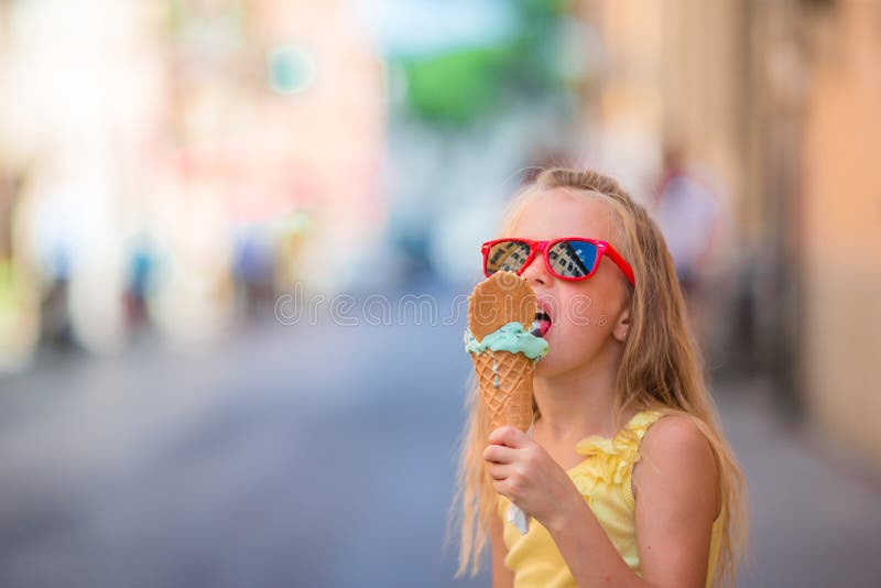 Bambina adorabile che mangia gelato all'aperto all'estate Bambino sveglio che gode del gelato italiano reale vicino a Gelateria a fotografia stock libera da diritti Bambina adorabile che mangia gelato all'aperto all'estate Bambino sveglio che gode del gelato italiano reale vicino a Gelateria a fotografia stock libera da diritti