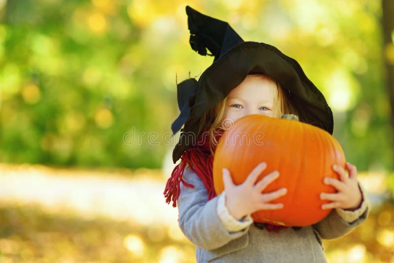 Bambina adorabile che porta il costume di Halloween divertendosi su una toppa della zucca il giorno di autunno fotografia stock Bambina adorabile che porta il costume di Halloween divertendosi su una toppa della zucca il giorno di autunno fotografia stock