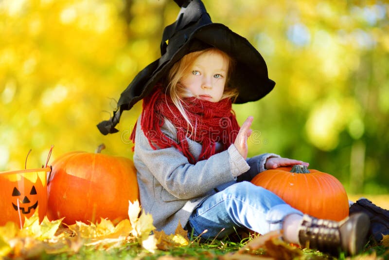 Bambina adorabile che porta il costume di Halloween divertendosi su una toppa della zucca il giorno di autunno immagine stock Bambina adorabile che porta il costume di Halloween divertendosi su una toppa della zucca il giorno di autunno immagine stock