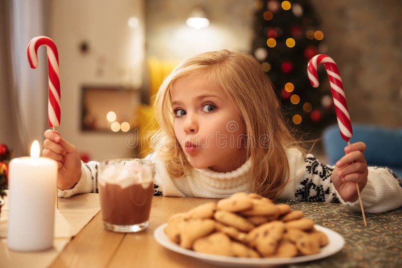 Bambina affascinante con due bastoncini di zucchero mentre avendo festivo fotografia stock Bambina affascinante con due bastoncini di zucchero mentre avendo festivo fotografia stock