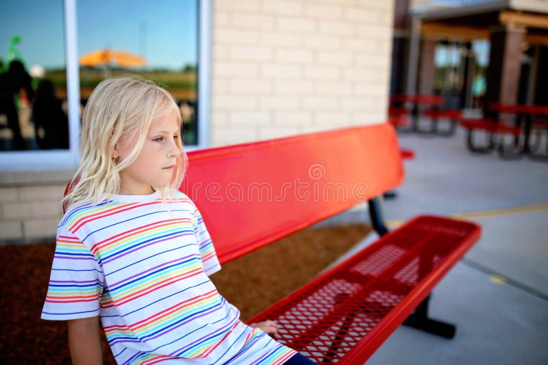Bambina che aspetta un amico con cui giocare nel parco giochi della scuola. Una ragazza dolce sta aspettando sulla panchina di un amico a scuola per chiederle di giocare sul parco giochi.