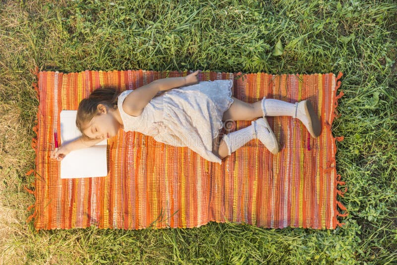 Bambina che dorme sul taccuino aperto che si riposa sulla coperta di picnic immagini stock libere da diritti