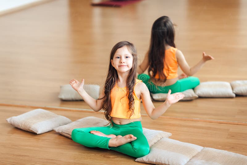 Bambina che fa yoga, ritratto di piccola yoga di pratica sorridente sveglia della ragazza, in un vestito arancio fotografie stock Bambina che fa yoga, ritratto di piccola yoga di pratica sorridente sveglia della ragazza, in un vestito arancio fotografie stock