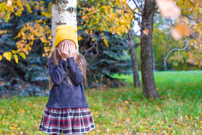 Bambina che gioca nascondino nella foresta di autunno