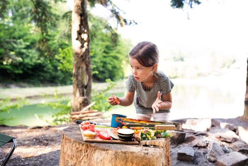 Bambina che si accampa nella foresta che mangia alimento arrostito immagine stock Bambina che si accampa nella foresta che mangia alimento arrostito immagine stock