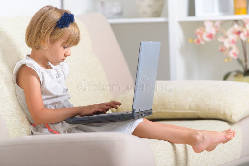 Bambina che si siede sullo strato con il computer portatile