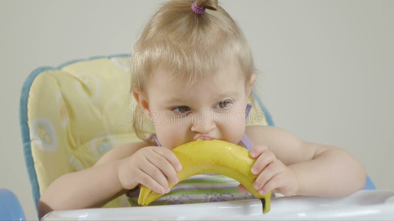 Bambina che si siede in una sedia del bambino che mangia una banana