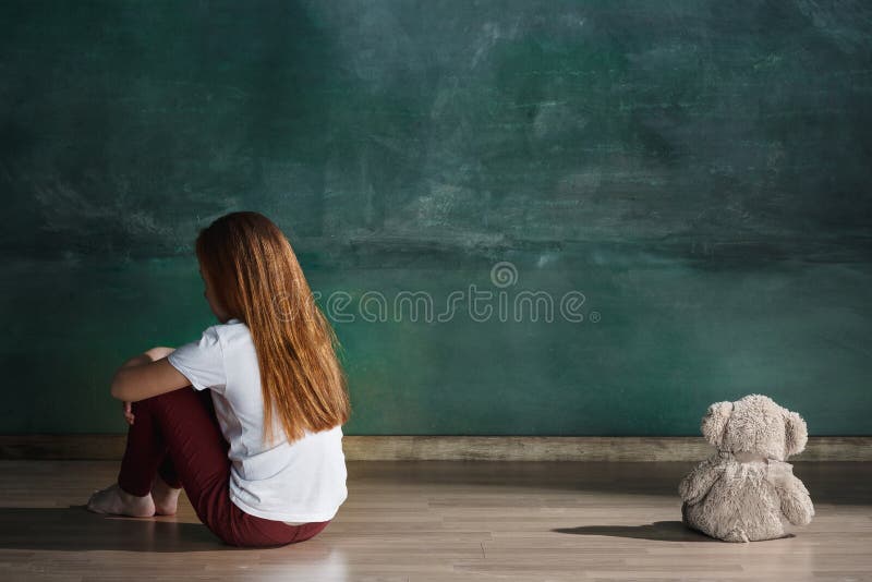 Bambina con l'orsacchiotto che si siede sul pavimento nella stanza vuota Concetto di autismo immagini stock Bambina con l'orsacchiotto che si siede sul pavimento nella stanza vuota Concetto di autismo immagini stock