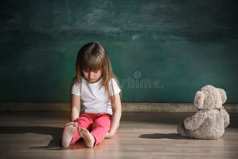 Bambina con l'orsacchiotto che si siede sul pavimento nella stanza vuota Concetto di autismo fotografie stock Bambina con l'orsacchiotto che si siede sul pavimento nella stanza vuota Concetto di autismo fotografie stock