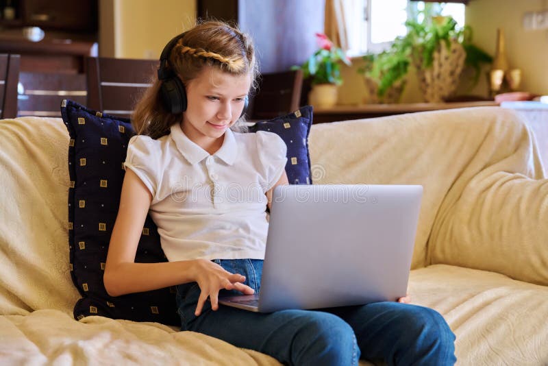 Bambina con le cuffie riposata a casa sul divano usando un portatile immagine stock