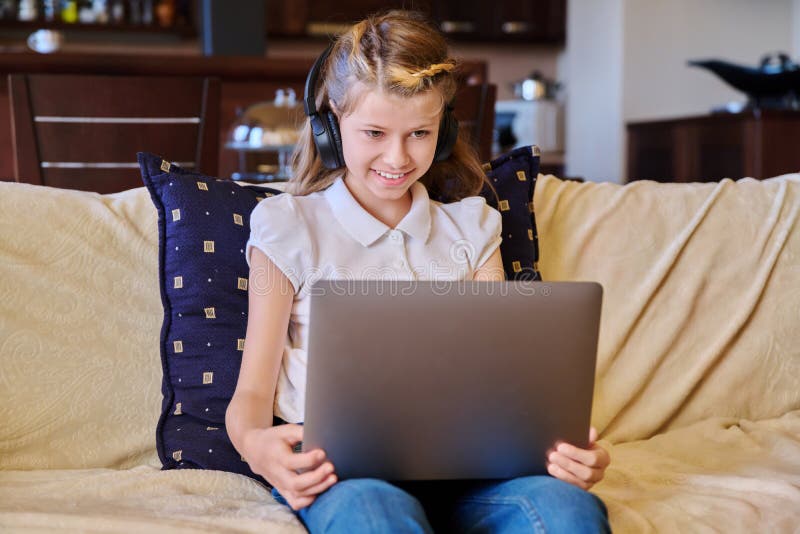 Bambina con le cuffie riposata a casa sul divano usando un portatile immagine stock