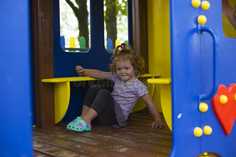 Bambina della testarossa in una casa di legno per i bambini sul campo da giuoco fotografia stock libera da diritti Bambina della testarossa in una casa di legno per i bambini sul campo da giuoco fotografia stock libera da diritti
