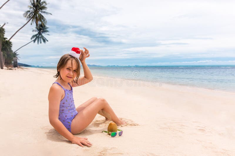 Bambina di Babbo Natale rossa che gioca con cocco sulla sabbia su una spiaggia tropicale Concetto estivo sulle vacanze tropicali immagini stock libere da diritti Bambina di Babbo Natale rossa che gioca con cocco sulla sabbia su una spiaggia tropicale Concetto estivo sulle vacanze tropicali immagini stock libere da diritti