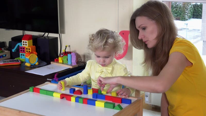 Bambina e babysitter che giocano con i blocchi di legno variopinti vicino alla piccola tavola stock footage