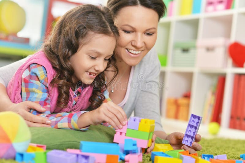 Bambina e sua madre che giocano con i blocchi di plastica variopinti immagini stock libere da diritti