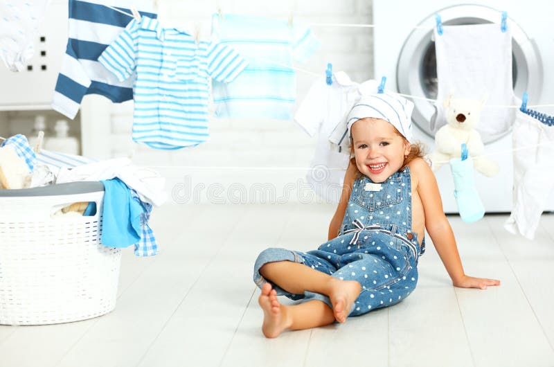 Bambina felice di divertimento del bambino per lavare i vestiti e le risate nel laund fotografia stock libera da diritti Bambina felice di divertimento del bambino per lavare i vestiti e le risate nel laund fotografia stock libera da diritti