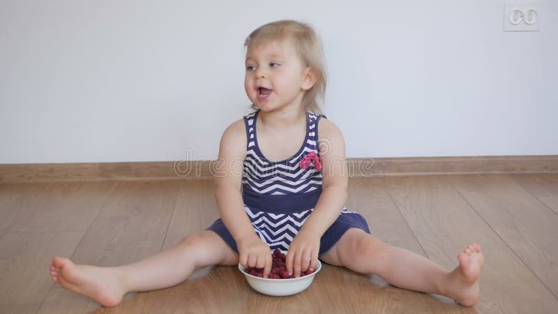 Bambina sedendosi su un cibo di legno del pavimento i lamponi rossi maturi