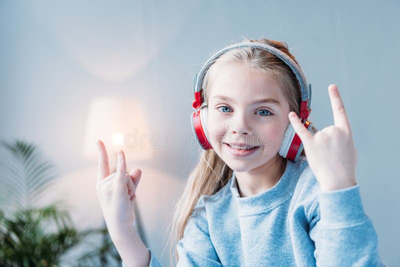 Bambina sorridente in cuffie che mostrano i segni della roccia immagine stock Bambina sorridente in cuffie che mostrano i segni della roccia immagine stock