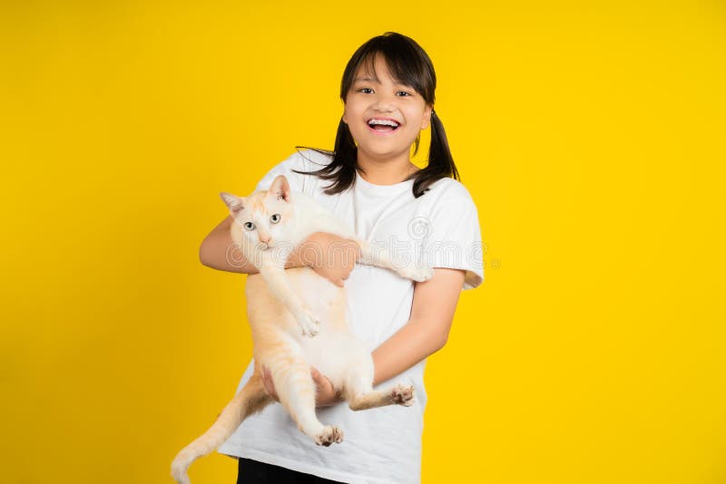 Bambina sorridente e felice di tenere in mano un gatto in uno studio isolato su sfondo giallo immagine stock