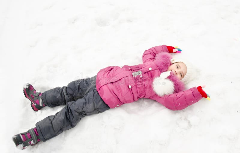 Bambina sorridente sveglia che si trova sulla neve nel giorno di inverno fotografia stock Bambina sorridente sveglia che si trova sulla neve nel giorno di inverno fotografia stock