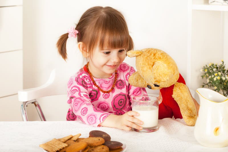 Bambina sveglia che dà bicchiere di latte all'orsacchiotto immagini stock Bambina sveglia che dà bicchiere di latte all'orsacchiotto immagini stock