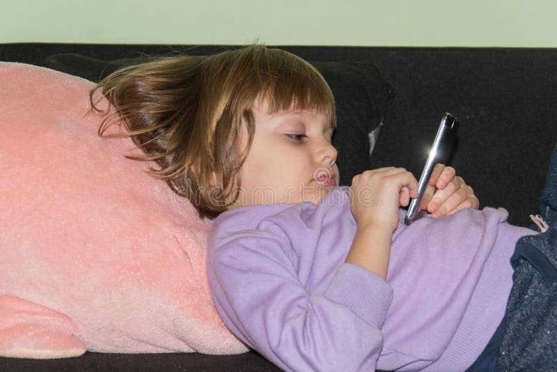 Bambina sveglia che si trova sul letto con il suoi maiale e telefono cellulare farciti del giocattolo fotografia stock libera da diritti Bambina sveglia che si trova sul letto con il suoi maiale e telefono cellulare farciti del giocattolo fotografia stock libera da diritti