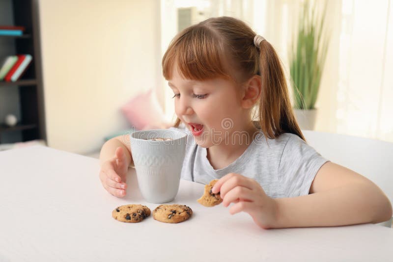 Bambina sveglia con la tazza della bevanda e dei biscotti caldi del cacao a casa fotografie stock libere da diritti Bambina sveglia con la tazza della bevanda e dei biscotti caldi del cacao a casa fotografie stock libere da diritti