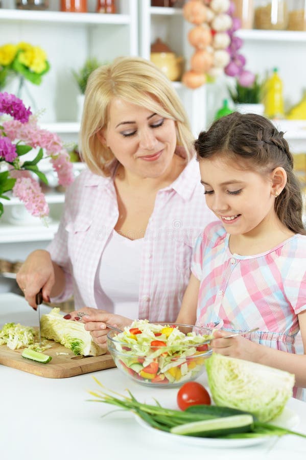 Bambina sveglia con sua madre che cucina insieme al tavolo da cucina fotografia stock libera da diritti Bambina sveglia con sua madre che cucina insieme al tavolo da cucina fotografia stock libera da diritti