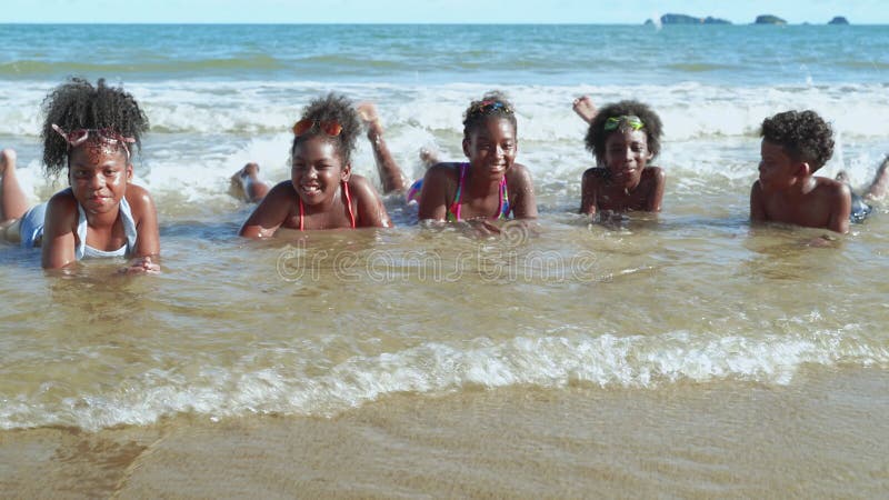 Bambini africani che giocano allegramente sulle onde marine sulla spiaggia durante una vacanza estiva