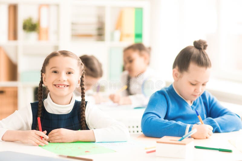 Bambini al banco. Ritratto della scolara sorridente che si siede allo scrittorio con il suoi classmte e disegno